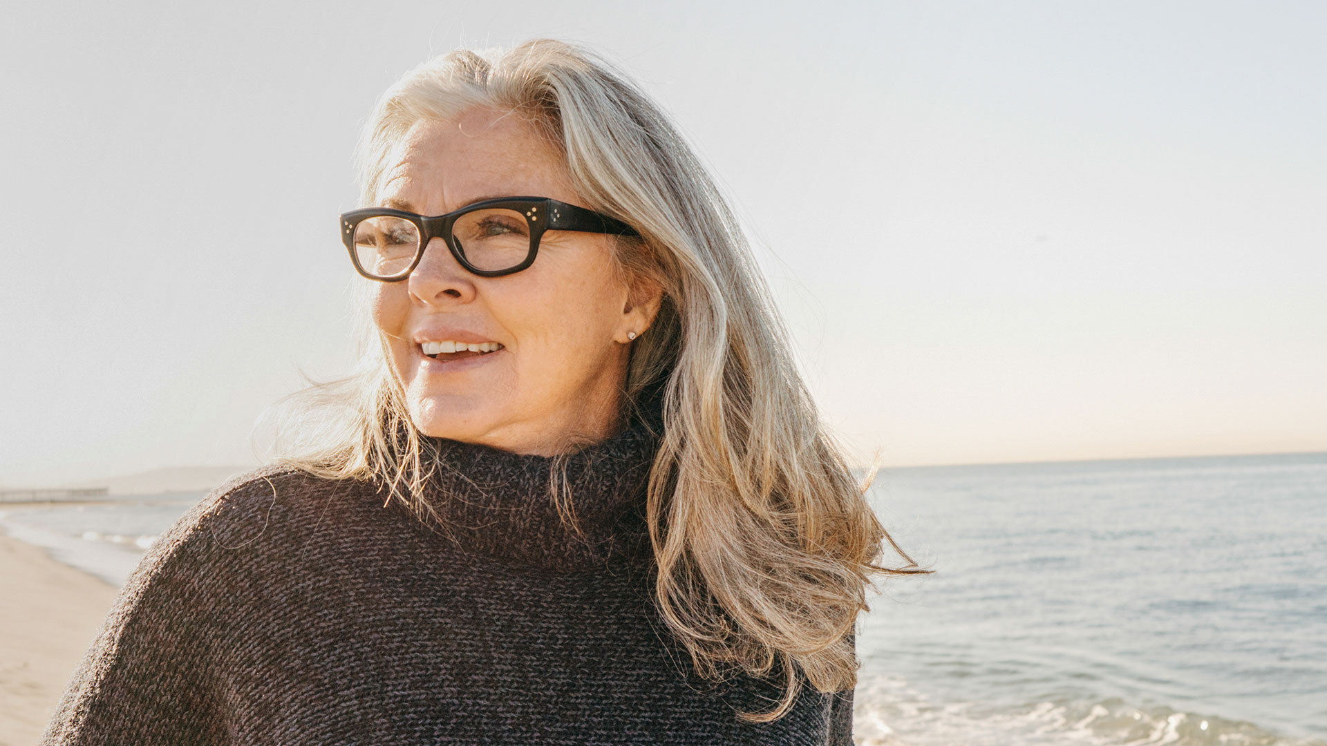 Eine Frau mit Brille steht am Strand und genießt die Sonne.