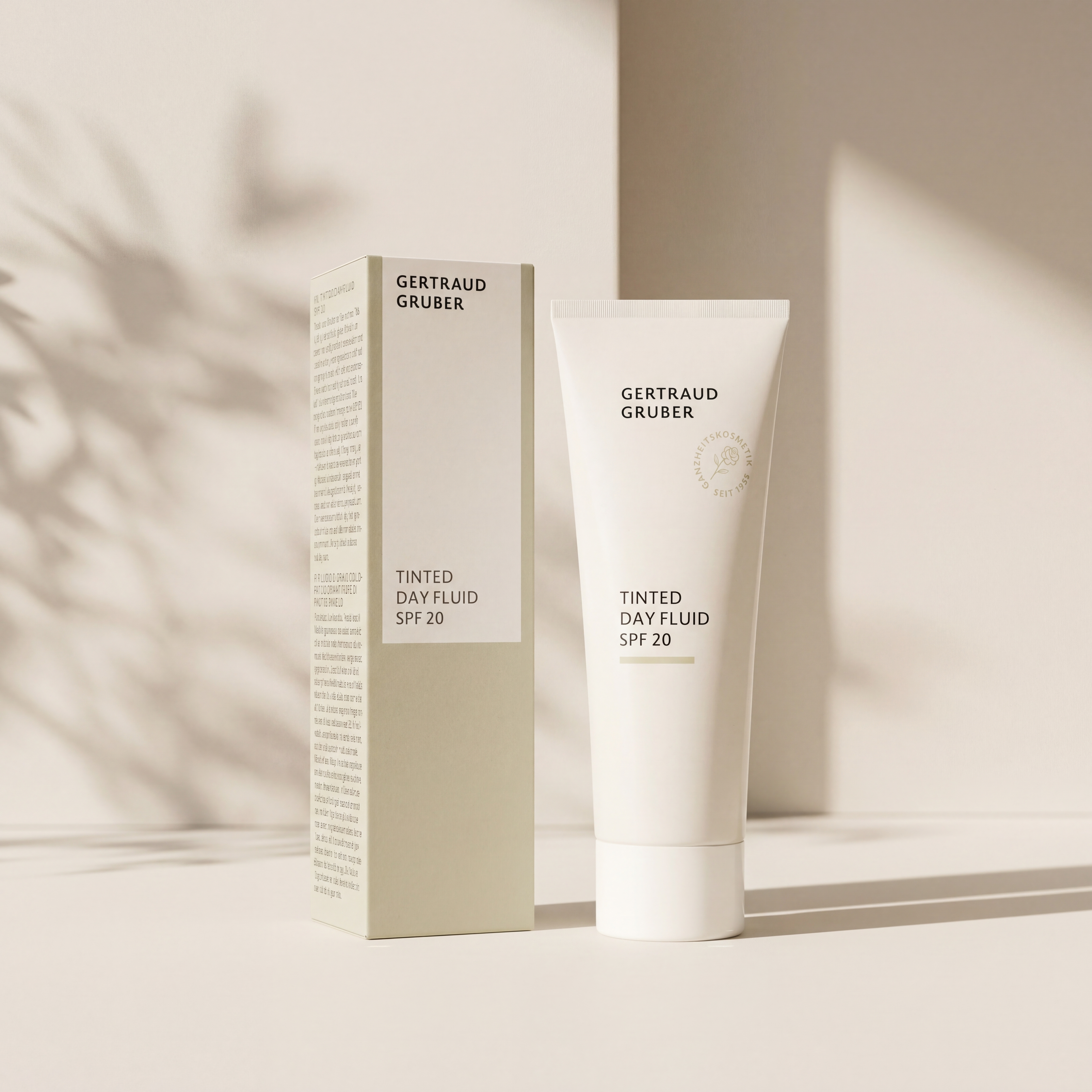 Weiße Tube Tinted Dayfluid LSF20 von Gertraud Gruber Kosmetik mit grüner Faltschachtel vor heller Wand mit sanften Schatten