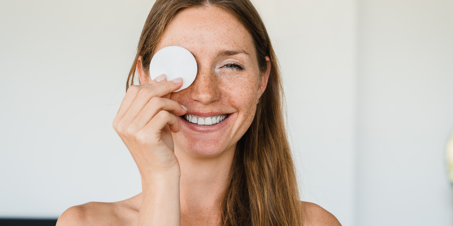 Lächelnde, junge Frau hält sich Abschminkpad vor ein Auge