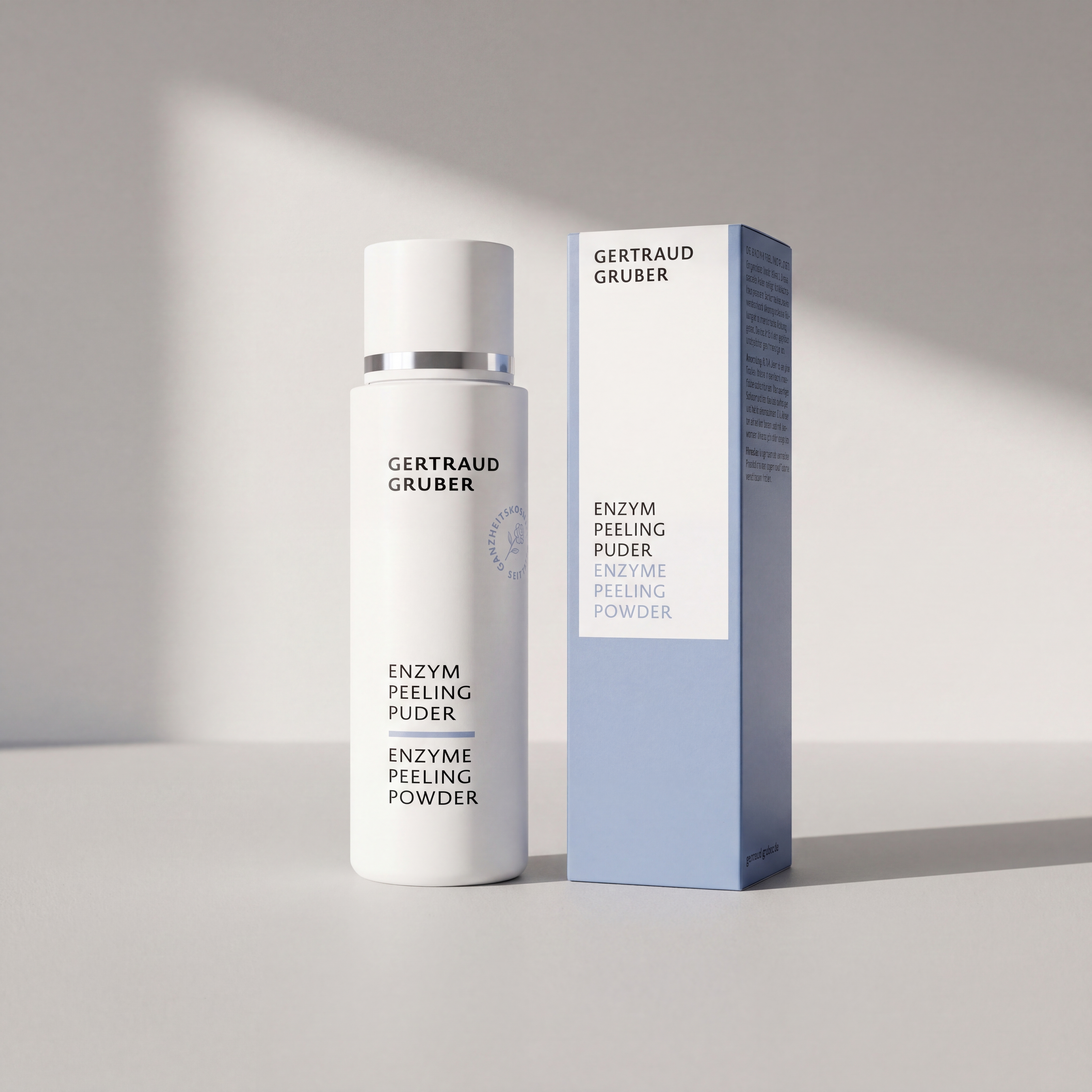 Weiße Tube Enzym Peeling Puder von Gertraud Gruber Kosmetik mit Faltschachtel  vor heller Wand mit Sonneneinstrahlung
