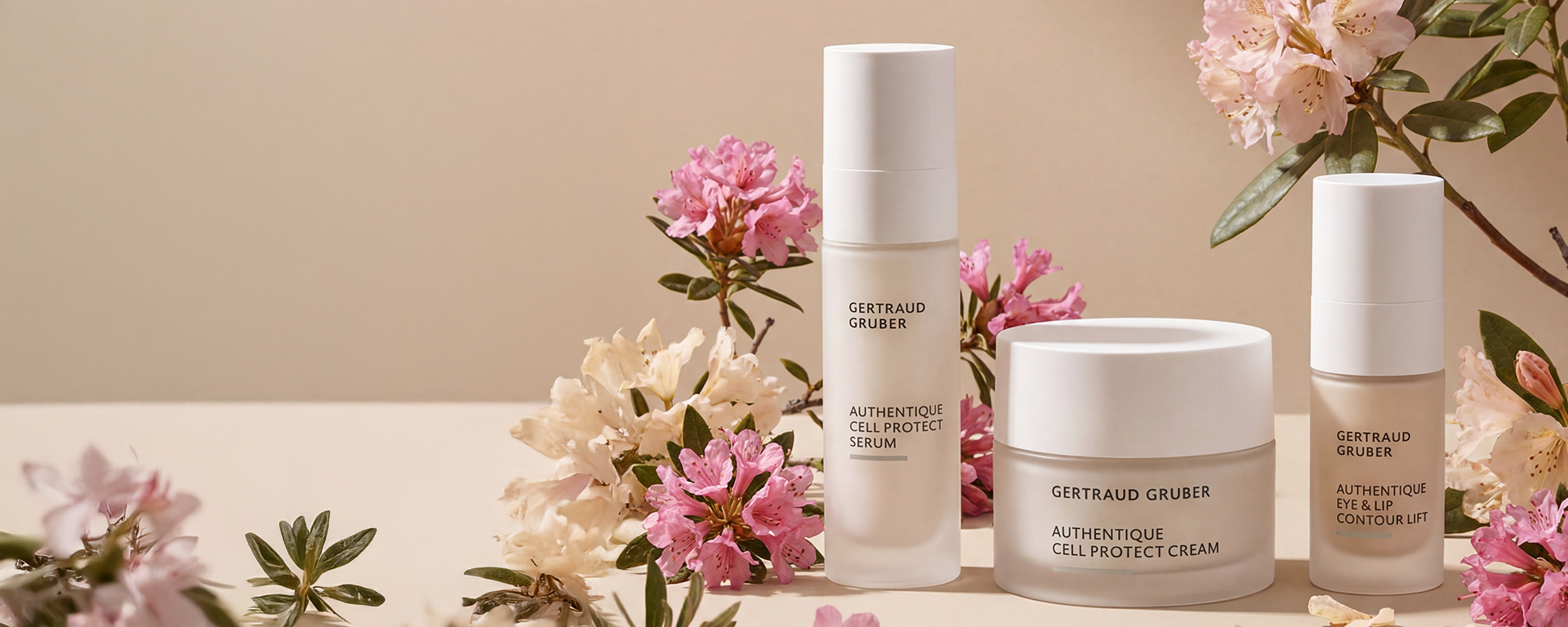 Authentique Serie von Gertraud Gruber Kosmetik: Serum, Creme und Eye & Lip Contour Lift in eleganten Glasflakons, umgeben von zarten rosé- und cremefarbenen Blüten