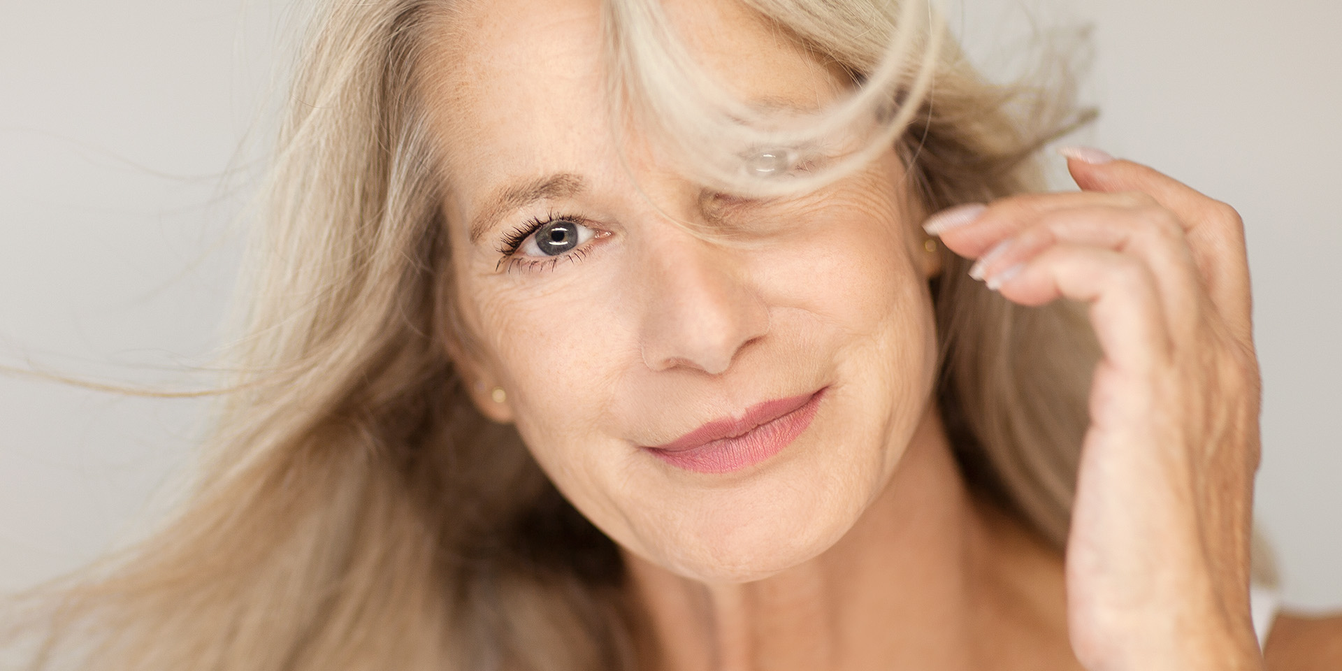 Frau mit wehenden Haaren schaut lächelnd in die Kamera