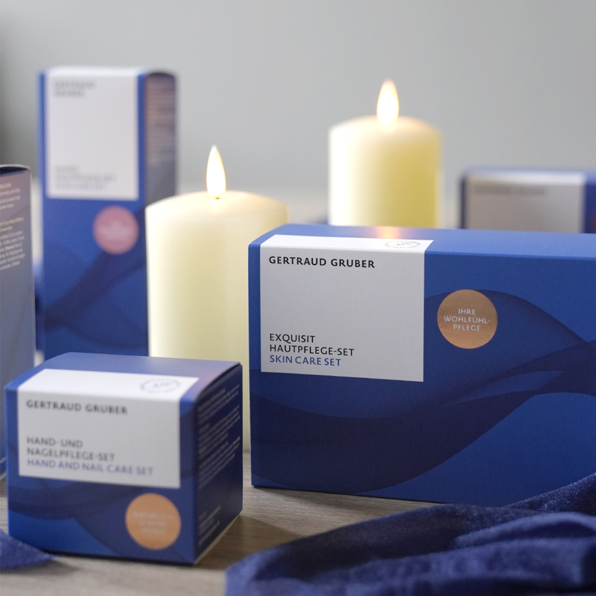 Gertraud Gruber Kosmetik Weihnachts-Sets in festlicher blauer Geschenkverpackung, stimmungsvoll arrangiert mit brennenden Kerzen.