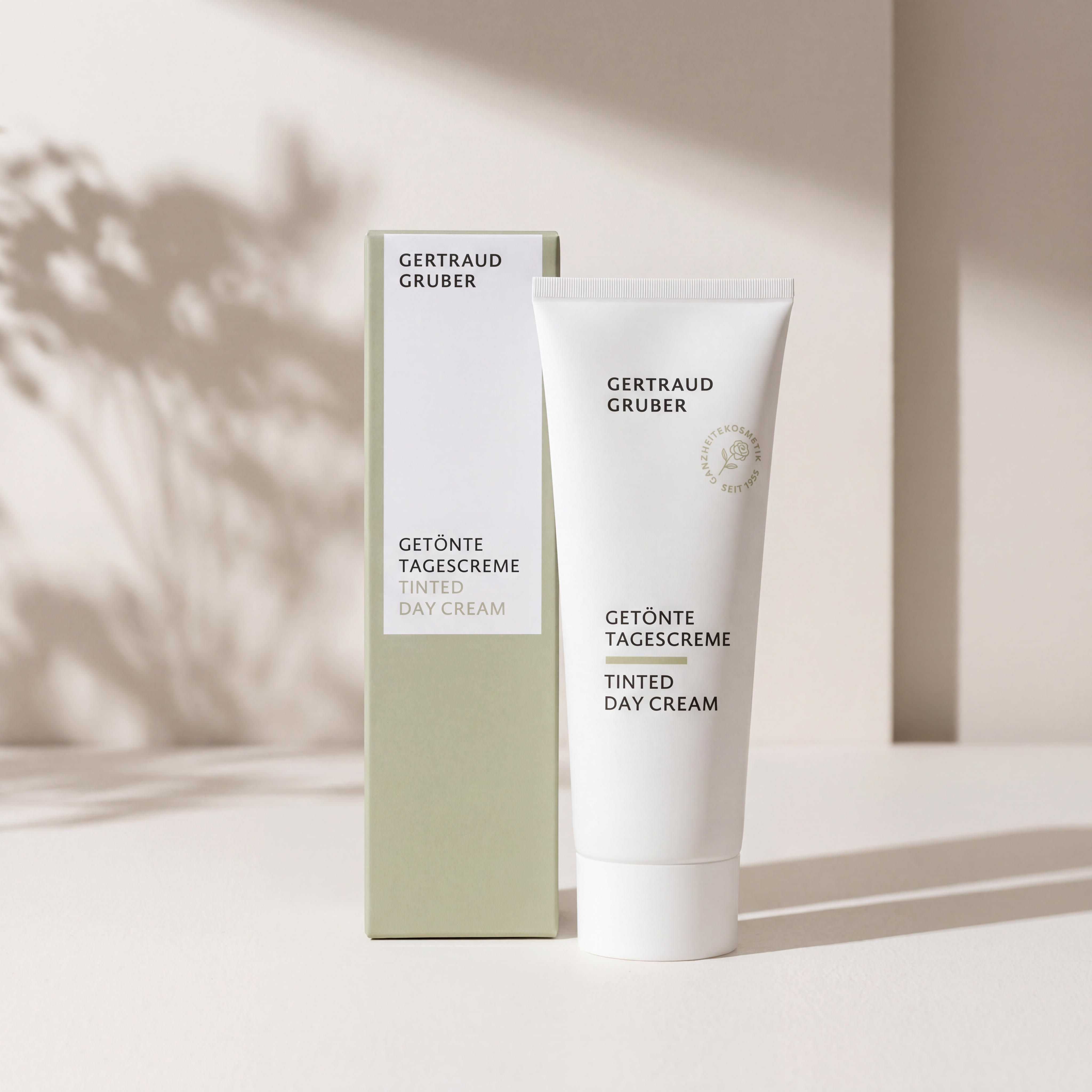 Weiße Tube Getoente Tagescreme von Gertraud Gruber Kosmetik vor heller Wand mit sanften Schatten mit grüner Faltschachtel