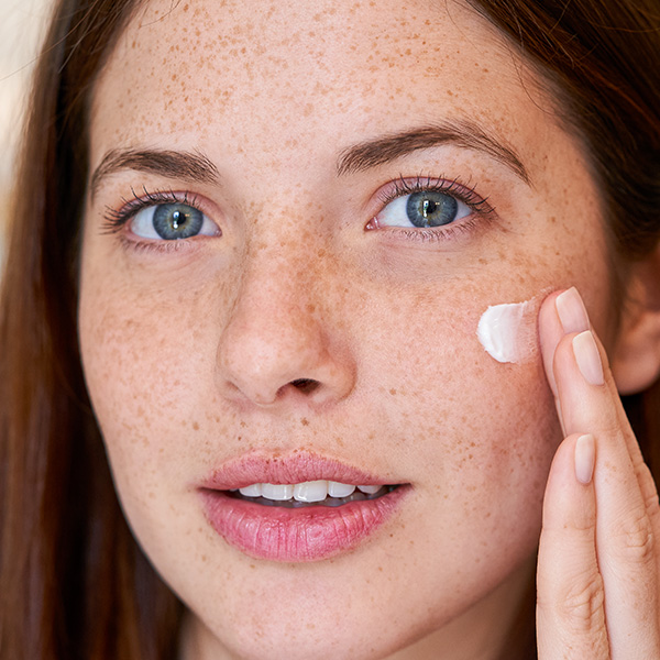 Junge Frau mit Sommersprossen trägt Gesichtscreme auf