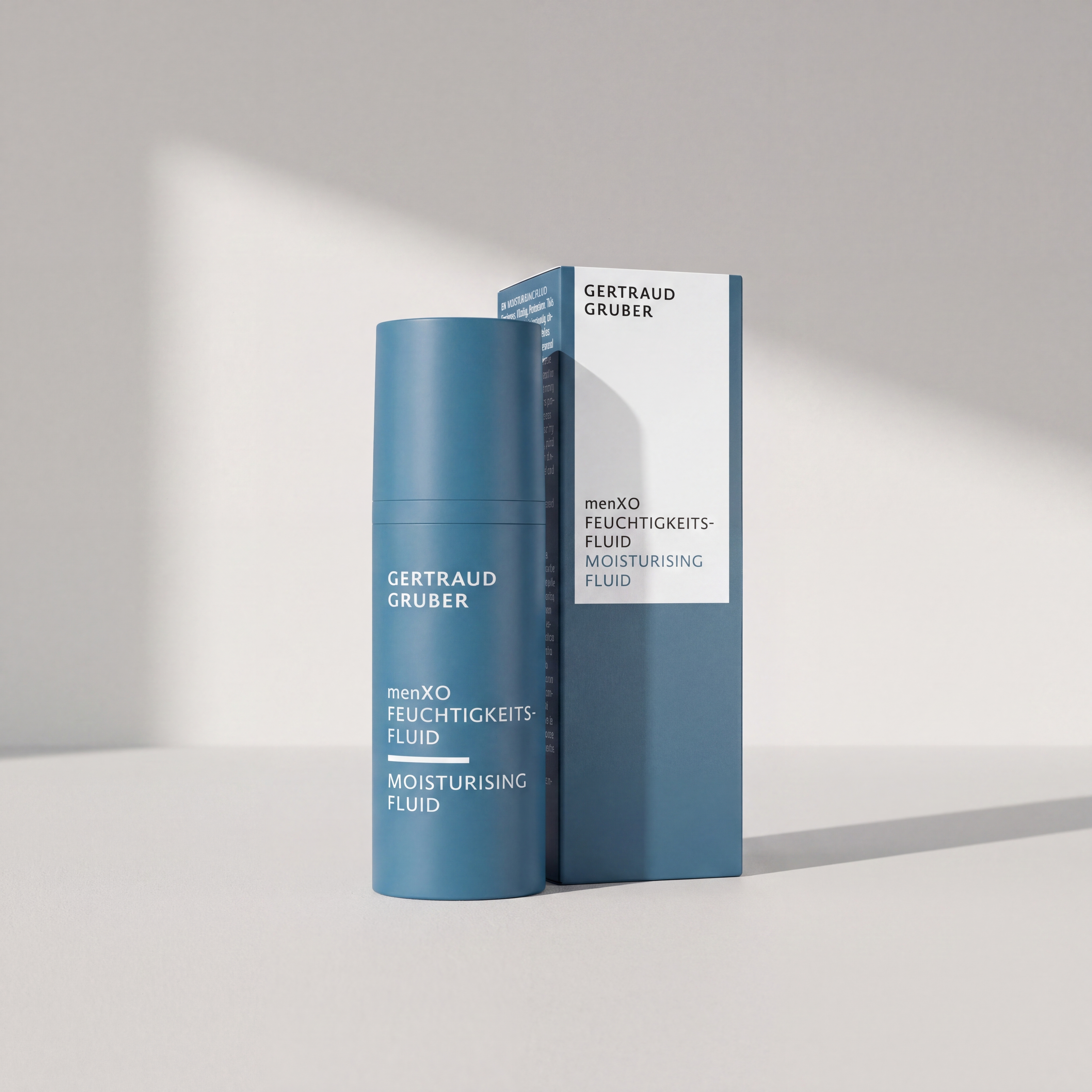 Blaue Pumpflasche menXO Feuchtigkeitsfluid mit Faltschachtel von Gertraud Gruber Kosmetik vor heller Wand mit sanften Schat