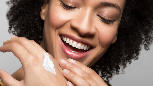 Lächelnde Frau trägt pflegende Creme auf Hand auf