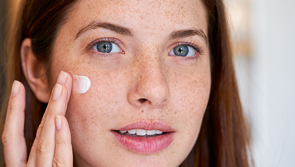 Frau trägt feuchtigkeitsspendende Gesichtscreme auf die Haut auf