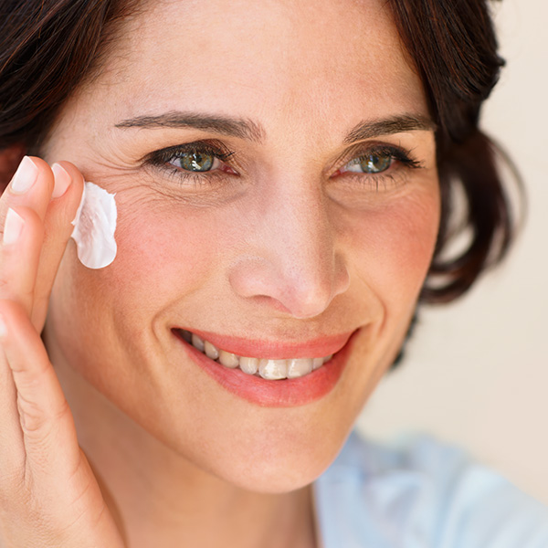 Frau trägt Creme auf ihr Gesicht auf und lächelt dabei