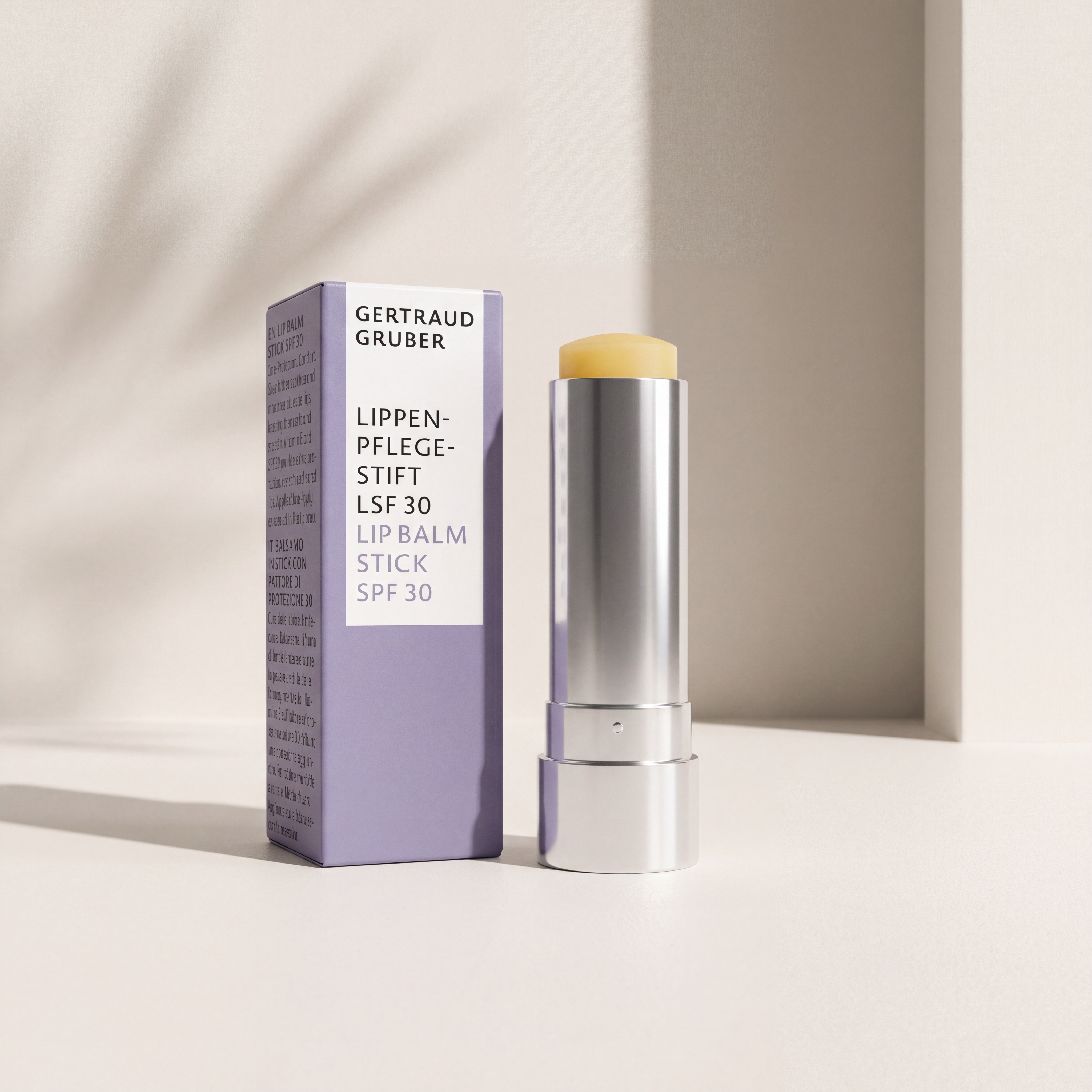 Gertraud Gruber Kosmetik Lippenpflegestift LSF30 mit Faltschachtel vor hellbeiger Wand