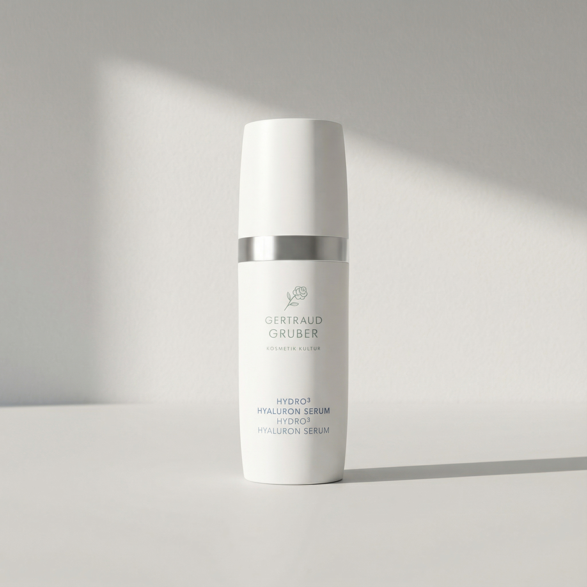 Weißer Spender mit Hydro³ Hyaluron Serum von Gertraud Gruber Kosmetik vor minimalistischer, heller Wand
