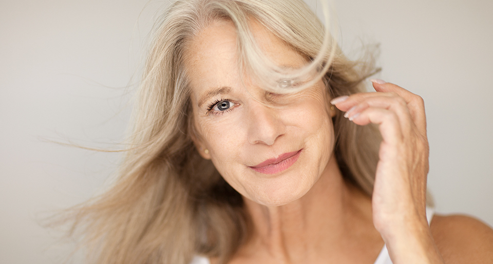 Frau mit wehenden Haaren schaut lächelnd in die Kamera