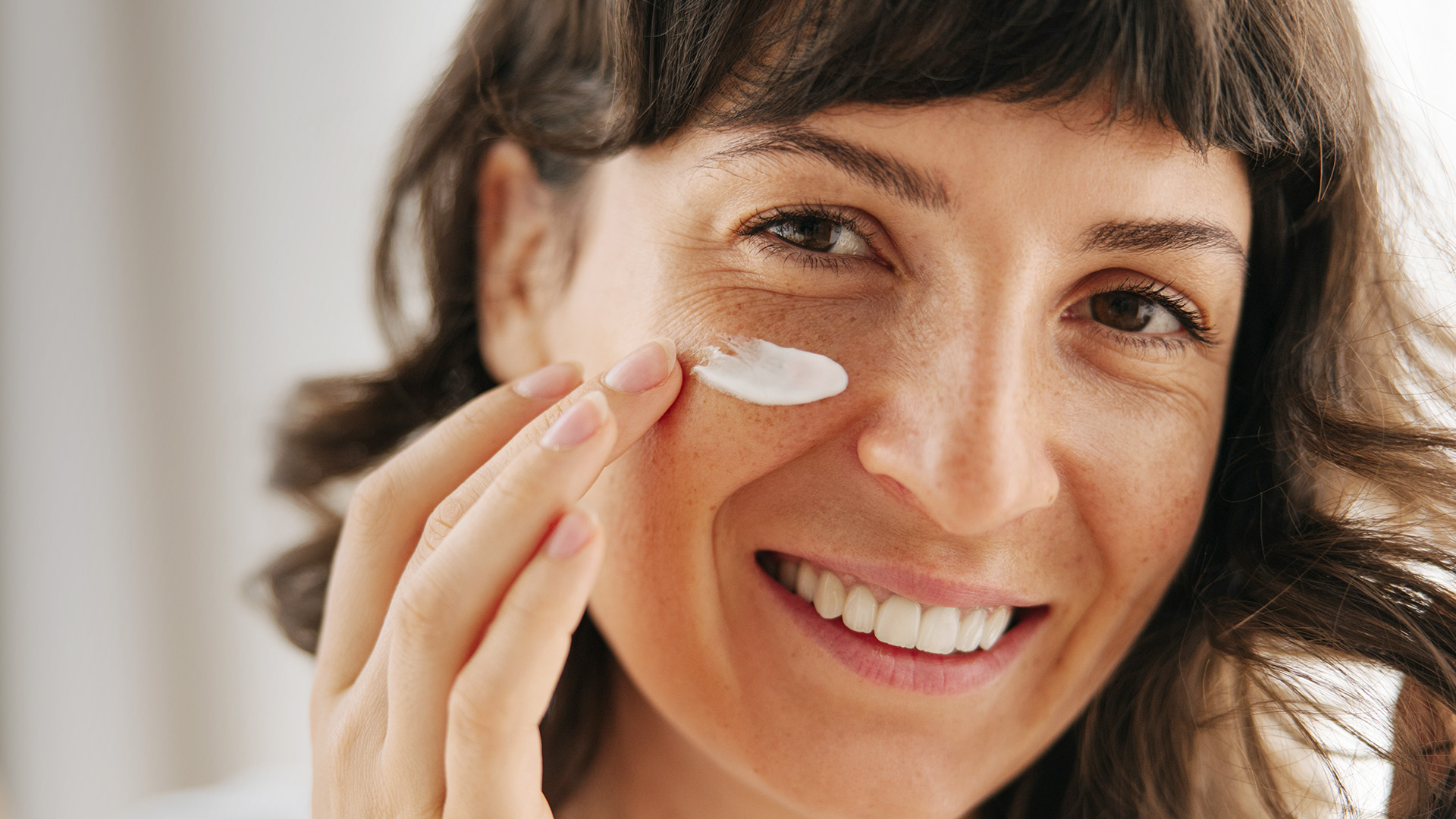 Close-Up von Frau die Creme aufträgt und in die Kamera lächelt