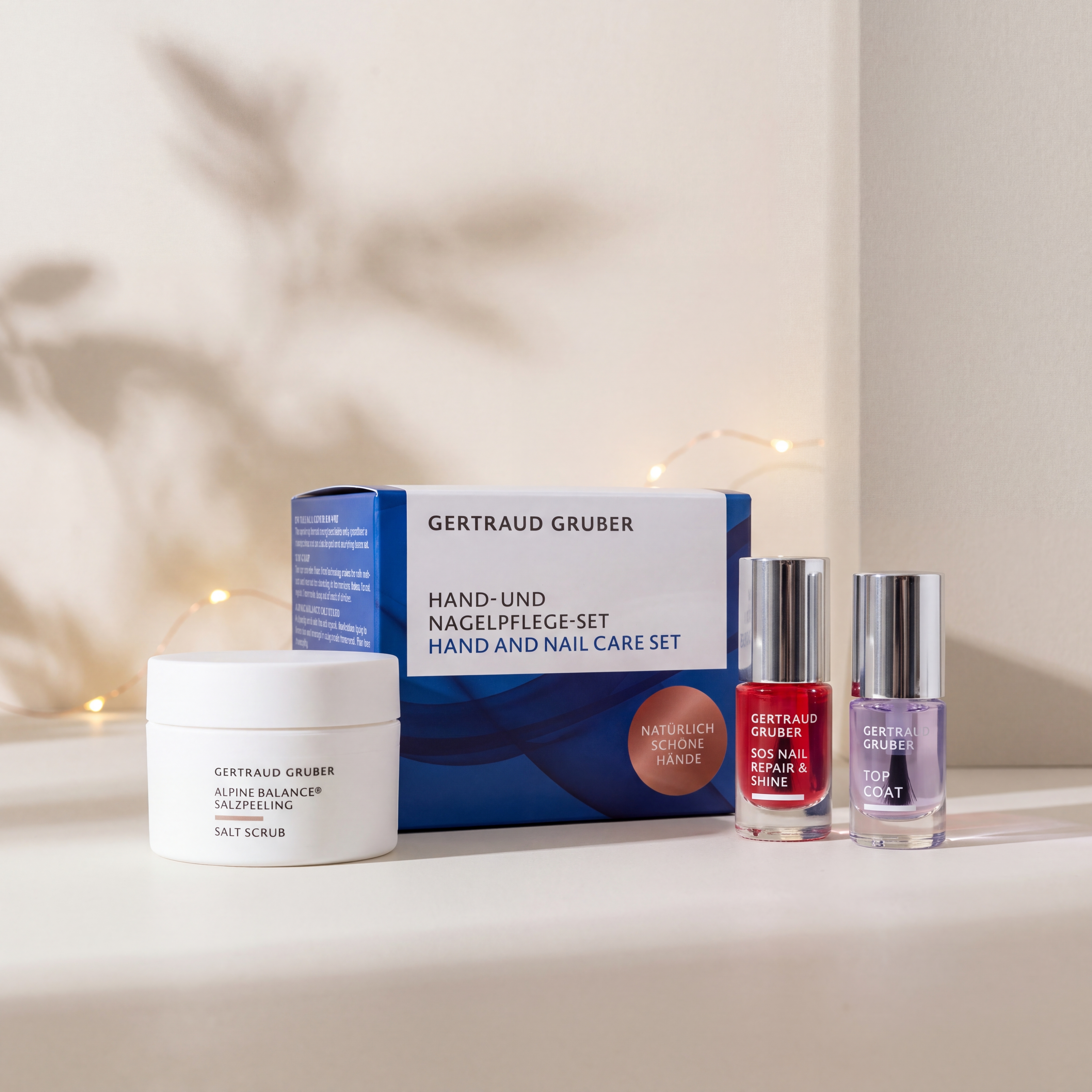 Hand- und Nagelpflege-Set von GERTRAUD GRUBER mit Alpine Balance Salzpeeling, SOS Nail Repair & Shine und Top Coat vor der Geschenkverpackung, stimmungsvoll inszeniert mit warmen Lichtern.