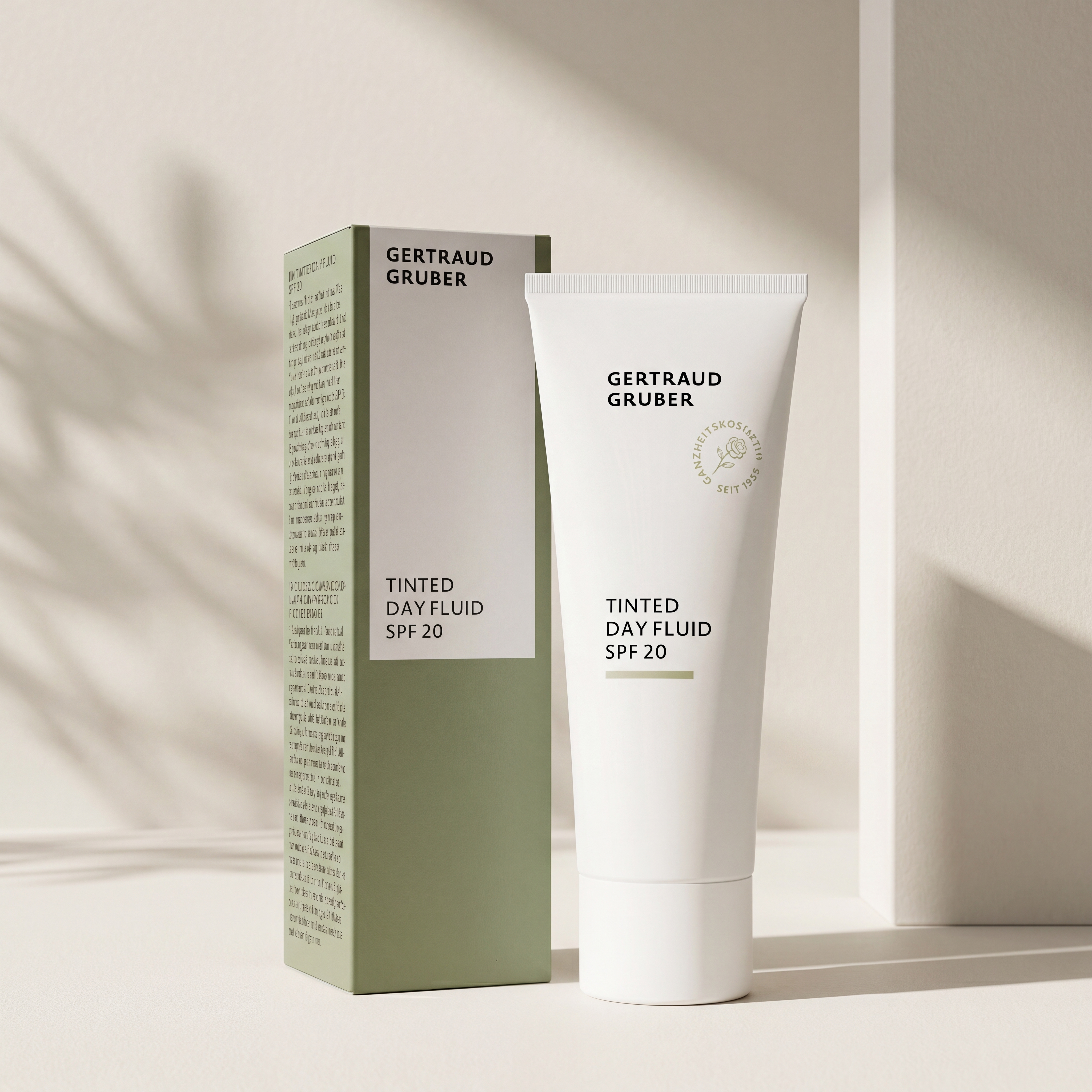 Weiße Tube Tinted Dayfluid LSF20 von Gertraud Gruber Kosmetik mit grüner Faltschachtel vor heller Wand mit sanften Schatt